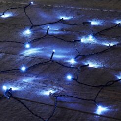 Niebieskie lampki choinkowe LED na ciemnozielonym przewodzie rozłożone na drewnianej powierzchni